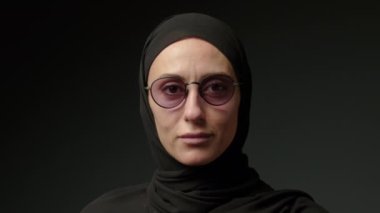 Portrait of beautiful young Arab muslim woman in black traditional hijab looking straight to camera and smiling. Close up of female pretty face with smile. Arabian headscarf. High quality 4k footage