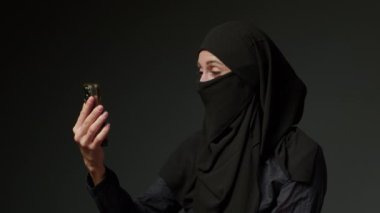 Woman in black muslim headscarf talking on mobile phone. Young arab muslim girl in headscarf hijab using smart phone, close up portrait of smiling middle eastern girl holding mobile smartphone.