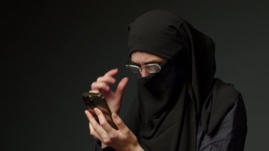 Woman in black muslim headscarf talking on mobile phone. Young arab muslim girl in headscarf hijab using smart phone, close up portrait of smiling middle eastern girl holding mobile smartphone.