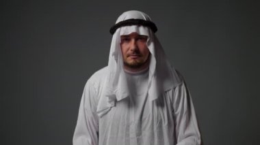 Portrait close up of successful arab man in traditional outfit, wearing white kandura and black agal looks at camera. Saudi, Emirati, Arab Businessman Concept. High quality 4k footage