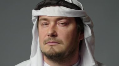 Portrait close up of successful arab man in traditional outfit, wearing white kandura and black agal looks at camera. Saudi, Emirati, Arab Businessman Concept. High quality 4k footage