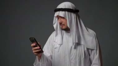 Authentic muslim businessman in traditional white kandura with beard using smartphone. Successful Saudi, Emirati, arab businessman concept. High quality 4k footage