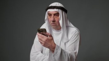 Elderly man with united arab emirates traditional clothes posing in a studio. Beautiful islamic portrait of portrait arab businessman kandur. Studio footage with different poses. High quality 4k