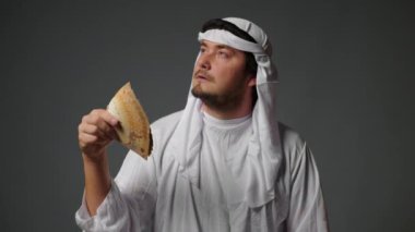 Successful Arabic sheikh in traditional clothes holds money in his hands on a gray background. Rich Arab man concept. High quality 4k footage