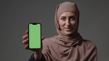Portre gülümseyen Arap Lübnanlı Müslüman kız tesettürlü kadın tesettürlü akıllı telefonu ön gösterim cep telefonunda yeşil ekranlı kamera reklamında uygulama servisi dijital cihaz reklamı.