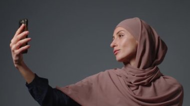 Portrait of happy muslim woman wearing hijab headscarf making selfie at phone, modern lifestyle, technology, smartphone usage, leisure time. High quality 4k footage