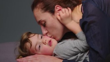 Close up shot of young mother is playing and kiss with her little girl in in a morning on gray background. Concept of children, baby, parenthood, childhood, life, maternity, motherhood.