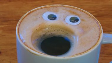 Smiling coffee man in a cup. Fragrant, lively coffee with eyes and mouth. Human face on fresh, milky coffee crema. High quality 4k footage