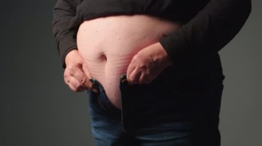 Göbekli bir kadın pantolon giyiyor. Şişman kadın çok küçük pantolonları bağlamaya çalışıyor. Yaşlı kadınlarda obezite. Yüksek kalite 4k görüntü