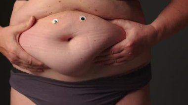 Aşırı kilolu yaşlı bir kadın göbeğini çimdikliyor, aşırı yemek yiyor, obezite yaşıyor. Kilolu insanların vücudunda normalden daha fazla yağ olması, vücut kitle indeksi, sağlıksız bir kavram. Yüksek kalite 4k görüntü