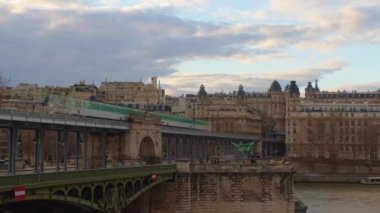Paris 'te Eyfel Kulesi ve Seine nehri yakınlarındaki şehir manzarasının zamanı. Metal, eski bir köprü. Metroyla giden ve insanların yürüdüğü. Arka planda bulutlar. Araba trafiği ve gün batımındaki insanlar..
