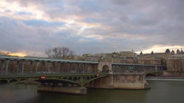 Paris 'te Eyfel Kulesi ve Seine nehri yakınlarındaki şehir manzarasının zamanı. Metal, eski bir köprü. Metroyla giden ve insanların yürüdüğü. Arka planda bulutlar. Araba trafiği ve gün batımındaki insanlar..