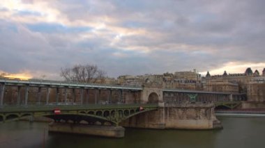 Paris 'te Eyfel Kulesi ve Seine nehri yakınlarındaki şehir manzarasının zamanı. Metal, eski bir köprü. Metroyla giden ve insanların yürüdüğü. Arka planda bulutlar. Araba trafiği ve gün batımındaki insanlar..