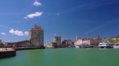La Rochelle Fransa 'daki limanda zaman aşımı. Okyanustaki ünlü Fransız şehri. Güneşli bir yaz günü, arka planda bulutlar hareket ediyor. Turist kalabalığı sokaklarda yürüyor. Yüksek kalite 4k görüntü