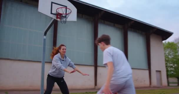 母親と息子は一緒にスポーツをしたり 学校の近くのバスケットボールコートでバスケットボールをしたりして自由な時間を過ごしています 家族の健康 健康的なライフスタイルを強化する バスケットボールの練習 — ストック動画