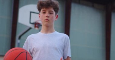 Basketbol sahasında elinde basketbol topu tutan bir çocuğun videosu. Elinde top, arkasında basketbol potası olan bir gencin sinematik çekimi..