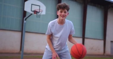 Şık bir saç stili olan genç bir adam kameraya bakıyor ve bir basketbol topuyla oynuyor. Okuldan sonra açık havada bir gencin portresi. Modern çocukların yaşam tarzı..