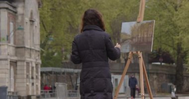 Seine nehrinin yakınında resim yapan bir kadın. Yaratıcı kadın sanatçı, Paris 'te sehpanın yanında dururken fırçayla resim yapıyor. Kadın sanatçı, satış sanatı, ilham.