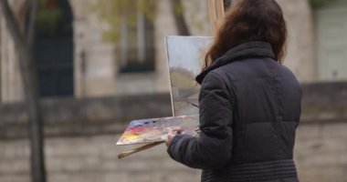 Seine nehrinin yakınında resim yapan bir kadın. Yaratıcı kadın sanatçı, Paris 'te sehpanın yanında dururken fırçayla resim yapıyor. Kadın sanatçı, satış sanatı, ilham.