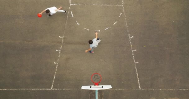 10代の少年がバスケットボールをするバスケットボールコートの空中ビュー ストリートバスケットボールのトップビュー バスケットボールトレーニングのドローンビデオ映像 — ストック動画