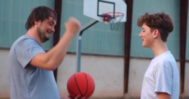 Spor ve arkadaşlık. Baba ve oğul basketbol oyuncuları birbirlerini sokak sahasında selamlıyorlar. Sarılma, yumruk tokuşturma, yan bakış, yavaş çekim..