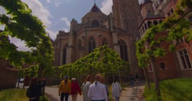 Bruges, Belçika, 26 Mayıs 2023: Şehir merkezindeki binalar. Şehirde yürüyen insanlar. İnsanlar ve turistler Pazar Meydanı 'nda yürüyorlar. Bruges Kulesi 'nin çan kulesi ve arka planda gotik binalar.