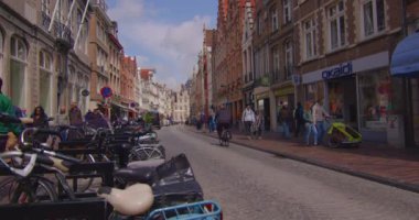 Bruges, Belçika, 26 Mayıs 2023: Şehir merkezindeki binalar. Şehirde yürüyen insanlar. İnsanlar ve turistler Pazar Meydanı 'nda yürüyorlar. Bruges Kulesi 'nin çan kulesi ve arka planda gotik binalar.