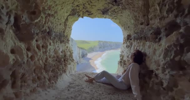 선글라스를 드레스를 Etretat 물에서 바위들의 배경에 맞서고 일몰에 곱슬머리가 매력적 — 비디오