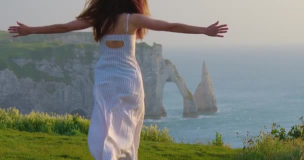 一个戴着太阳镜 穿着连衣裙的女人站在悬崖边上 面对着埃特里特水中著名岩石的背景 日落时分一头卷曲长发的漂亮女人的慢动作 — 图库视频影像