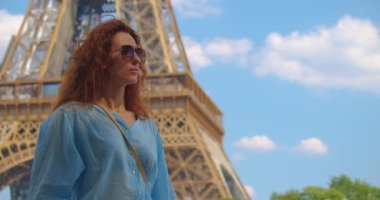 Gülümseyen turist kadın ünlü Eyfel Kulesi 'nin simgesine bakıyor. Fransa 'nın başkentinde tatilde olan bir kadın Eyfel Kulesi' nin etrafında dolaşıyor. Eyfel Kulesi en çok fotoğraflanan simgedir.