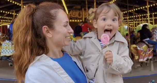 Little Girl Her Mothers Arms Eats Colorful Candy Amusement Park — Stock Video