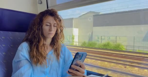 Žena Kudrnatými Vlasy Sedí Vlaku Dívá Mobilní Telefon Slunečného Dne — Stock video