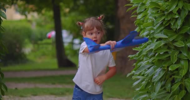 赤ちゃんは青い飛行機のおもちゃを手に持っている 自然と誠実な子供の感情 夏の公園で少女の肖像画 人生を楽しむ子供のクローズアップ — ストック動画