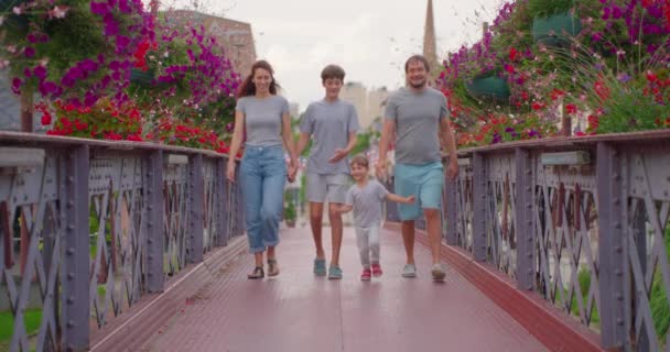 积极的父母和孩子们带着五彩缤纷的花朵走在桥上 快乐的家庭会花时间在户外 一对快乐的夫妇带着孩子在公园里散步 笑着让家人在外面开心 — 图库视频影像
