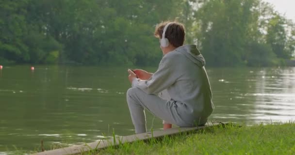 Мальчик Подросток Слушает Расслабляющую Музыку Наушниках Сидя Парке — стоковое видео