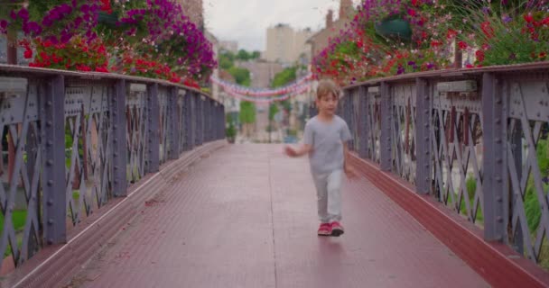 一个带着五彩缤纷花朵的积极小女孩走在桥上 快乐的家人在户外消磨时间 — 图库视频影像