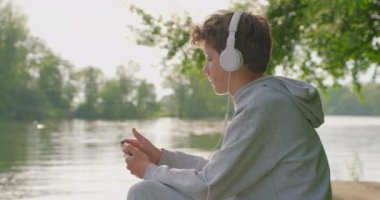 Genç çocuk parkta otururken kulaklıkla müzik dinliyor..