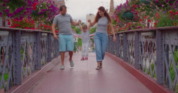 Позитивные Родители Дети Ходят Мосту Красочными Цветами Счастливая Семья Проводит — стоковое видео