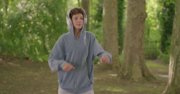 ティーンエイジャーは夏に屋外でヘッドフォンでトレンディな音楽を聞く 十代の頃の13歳の少年が両親と対立している ティーンエイジャーと親の関係 — ストック動画