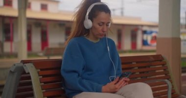 İstasyonda tren beklerken kulaklıkla müzik dinleyen bir kız..