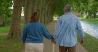 Parkta birlikte yürüyen bir çift olgun insan. Adam bir kadına nazikçe sarılıyor..