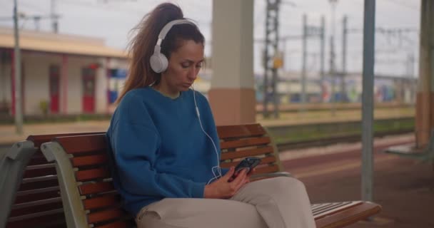 Lány Zenét Hallgat Fejhallgatóval Miközben Vonatra Vár Állomáson — Stock videók