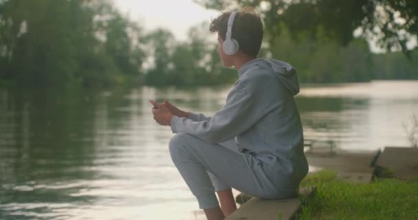 Genç Yaşta Kulaklık Takıyor Nehir Kenarında Müzik Dinliyor — Stok video