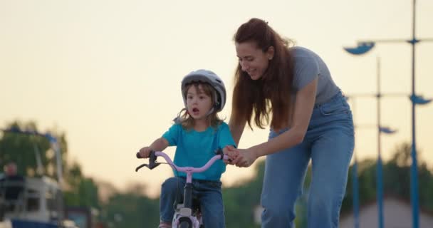 ママは娘に自転車に乗るように教える 幸せな家族の子供時代の夢の概念 母と娘は公園で自転車に乗ることを学びます ハッピーファミリーはアウトドアの日光のために行く — ストック動画