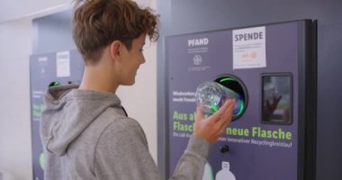 Genç bir genç, Almanya 'da para karşılığında bir makineye plastik boş şişeler veriyor. Plastik geri dönüşüm, çevre ekolojisi, gelecek nesiller için ekolojinin korunması.