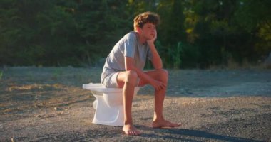 Genç adam tuvalette oturur ve günbatımının arka planını düşünür.. 