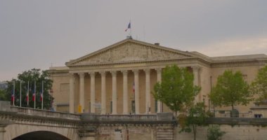 Fransız ve AB bayrakları dalgalanan Fransız Ulusal Meclisi binası - Paris, Fransa. Seine Nehri boyunca yelken açan bir yolcu gemisinden görüntü.