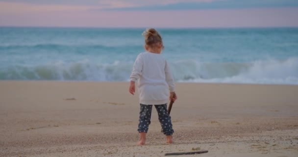 砂の中の小さな女の子は日没 リアビュー クローズアップで砂浜に描きます — ストック動画