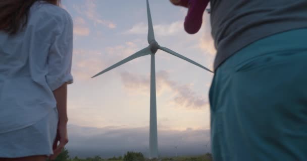 一个男人背着他的孩子 和他的妻子在风力农场散步时被枪杀了 快乐的家庭在更环保的生活中享受美丽的落日和清新的空气 — 图库视频影像
