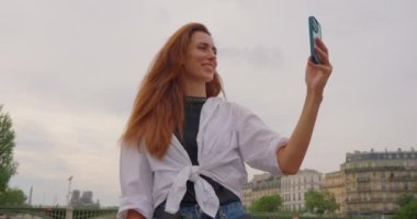 Sen nehri boyunca seyreden bir kız Paris manzarasının arka planında kendi fotoğrafını çekiyor..